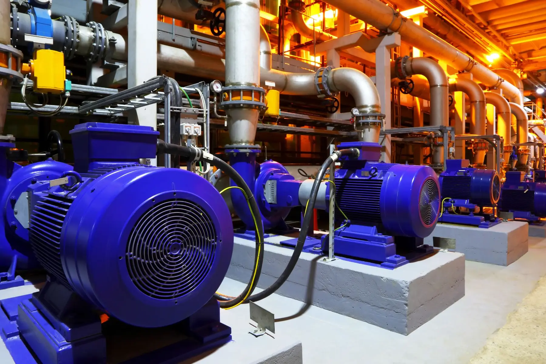 A row of blue electric motors driving pumps on concrete plinths in an industrial plant